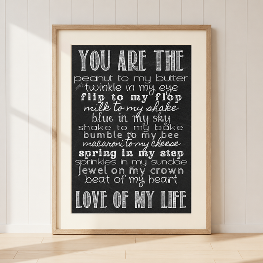Romantic "You Are The Love Of My Life" typography print featuring sweet love sayings in white text on a black chalkboard background, displayed in a light oak frame with warm ivory mount.