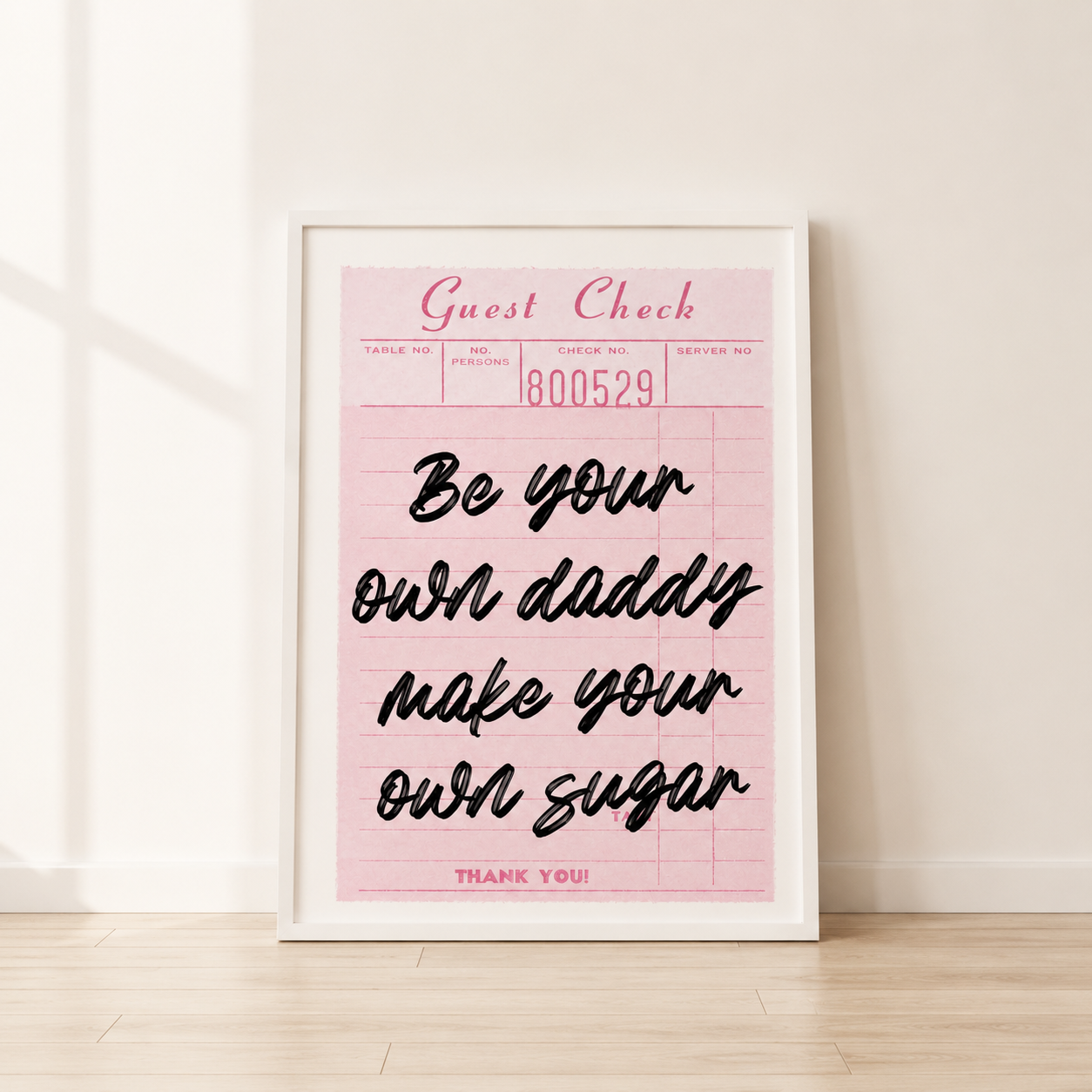 Framed pink print with black text on a light wooden floor.