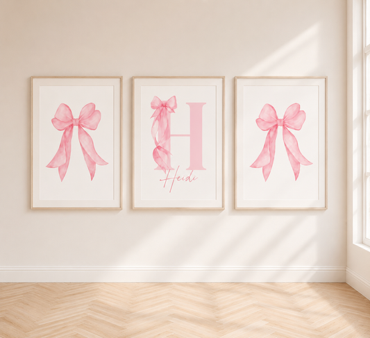 Personalised pink bow wall art prints displayed in neutral oak frames above a girls bedroom bed with soft blush decor.