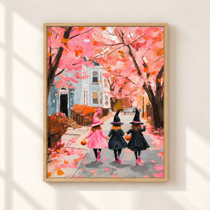 A framed art print depicting three children in witch hats and dresses walking down a street under pink autumn trees, shown hanging on a light beige wall with soft window shadows.