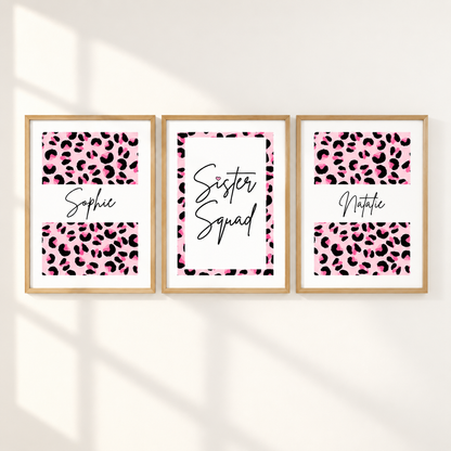 Three framed personalized prints with pink leopard print and black text hang on a white wall. The left print says 'Sophie', the center says 'Sister Squad', and the right says 'Noticia'.