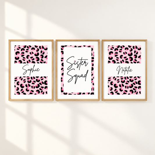 Three framed personalized prints with pink leopard print and black text hang on a white wall. The left print says 'Sophie', the center says 'Sister Squad', and the right says 'Noticia'.