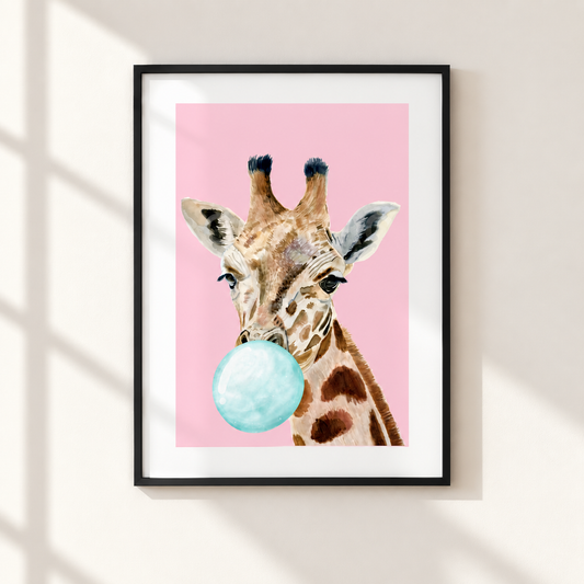 Framed wall art featuring a watercolor-style giraffe with a light blue bubblegum bubble against a pink background, hung on a beige wall with soft window-shadow lighting.