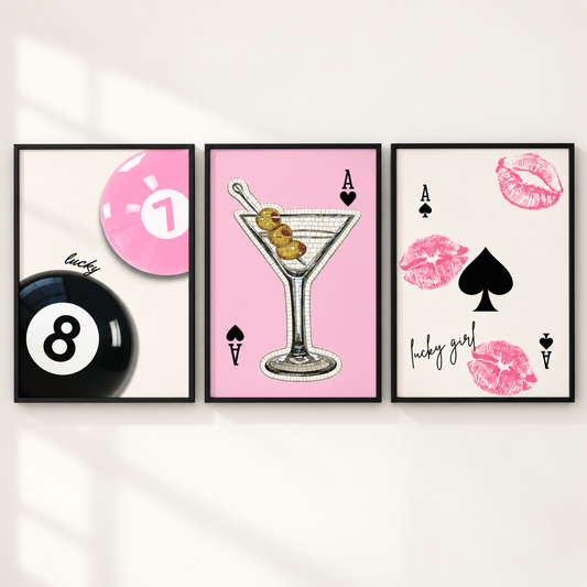 Three framed wall art prints displayed side by side on a light wall. The left print shows a pink 1-ball and a black 8-ball with the word 'lucky'; the center print shows a martini glass with olives on a pink background with 'A' and spade symbols; the right print shows pink lip marks, a black spade, 'A' and 'V' symbols, and the phrase 'lucky girl'.