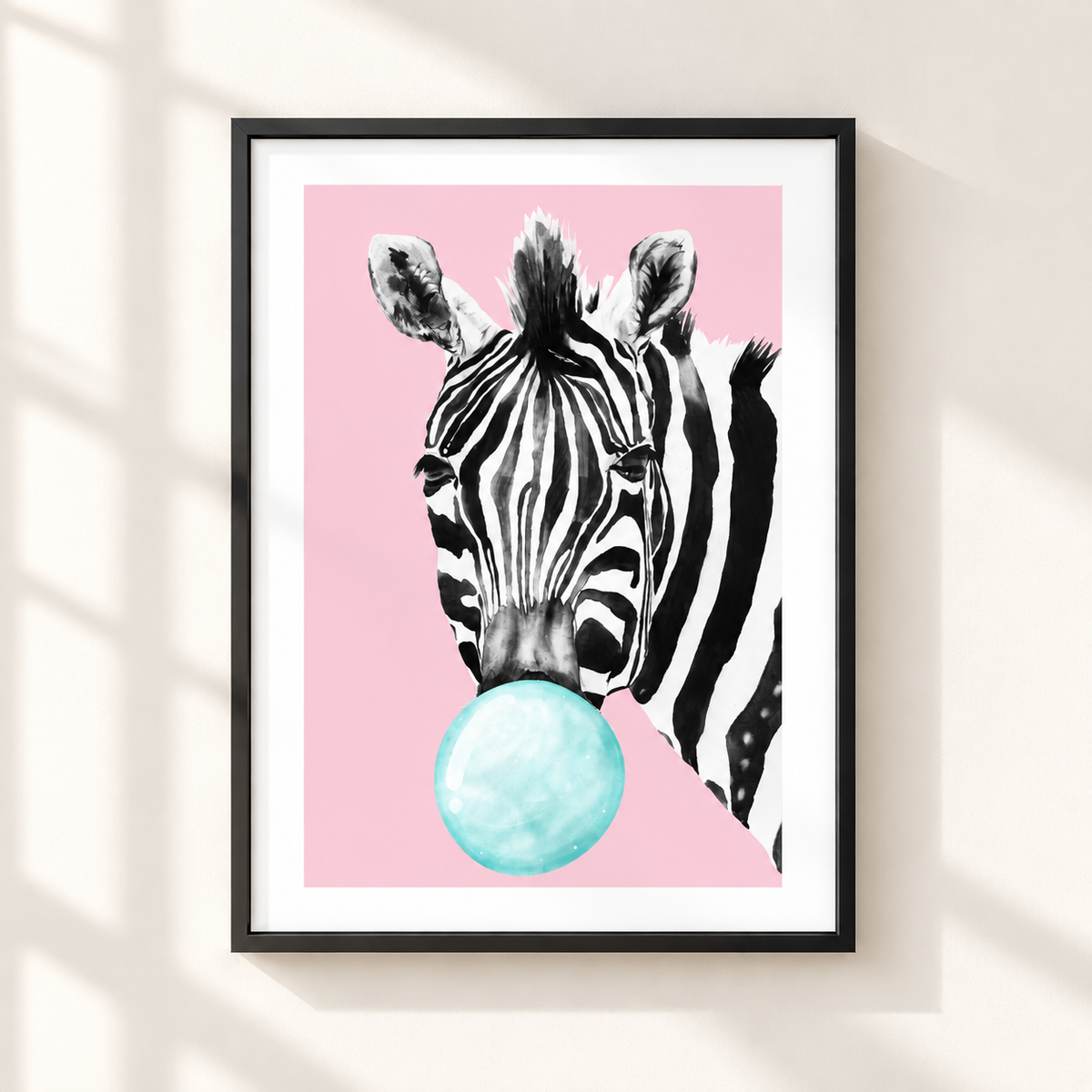 Framed wall art featuring a black-and-white zebra head blowing a light blue bubblegum bubble against a pink background, shown hanging on a beige wall with soft window-shadow lighting.