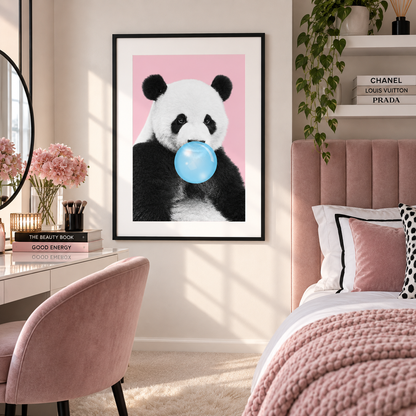A framed wall art print featuring a panda holding a blue bubblegum bubble against a pink background, displayed in a styled bedroom with a pink upholstered bed, chair, desk, and shelves.