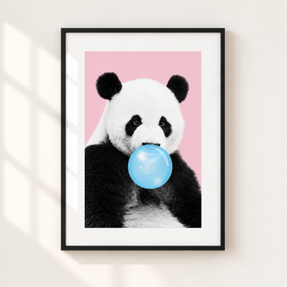 A framed art print featuring a black and white panda holding a light blue bubblegum bubble against a solid pink background, mounted on a light beige wall with soft window shadow overlays.