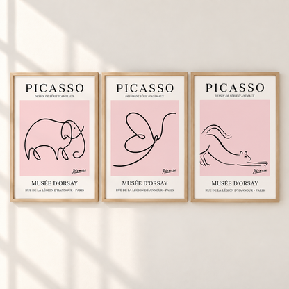 Three framed minimalist Picasso art prints hang side by side on a light wall with soft shadow overlays. Each print has a light pink square background, black line drawings (elephant, butterfly, horse), and white text reading PICASSO and MUSÉE D'ORSAY.