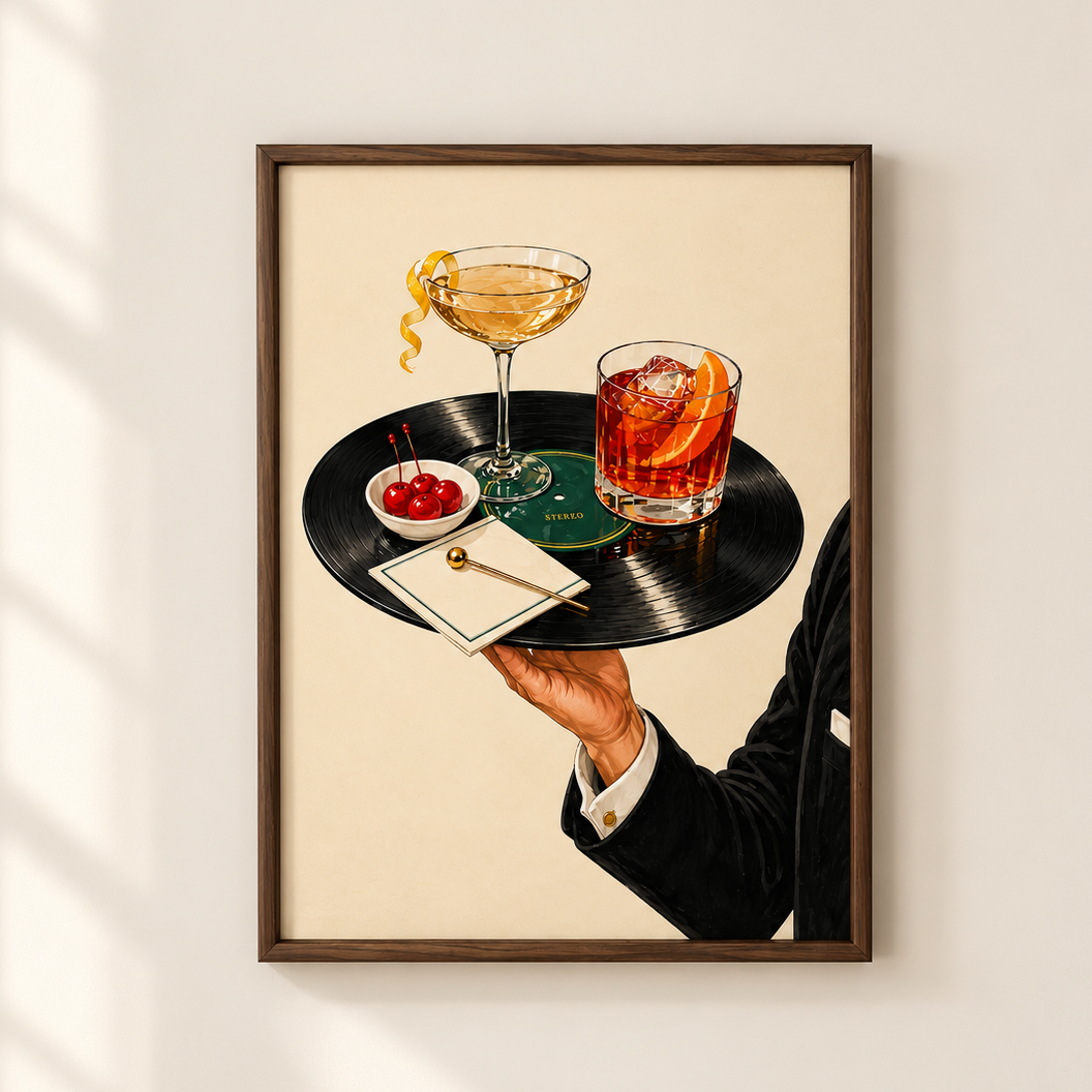 A framed art print hanging on a light beige wall, depicting a bartender in a black suit holding a black vinyl record tray with a martini glass, an orange cocktail, cherries, and a small gold spoon. The print is shown with soft window shadow overlays on the left side.