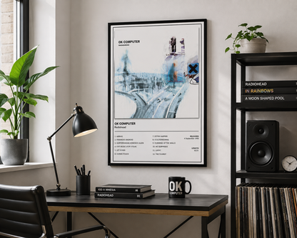 A framed art print featuring the OK Computer album cover design, hanging on a wall in a modern, styled home office setting with a desk, lamp, and shelving.