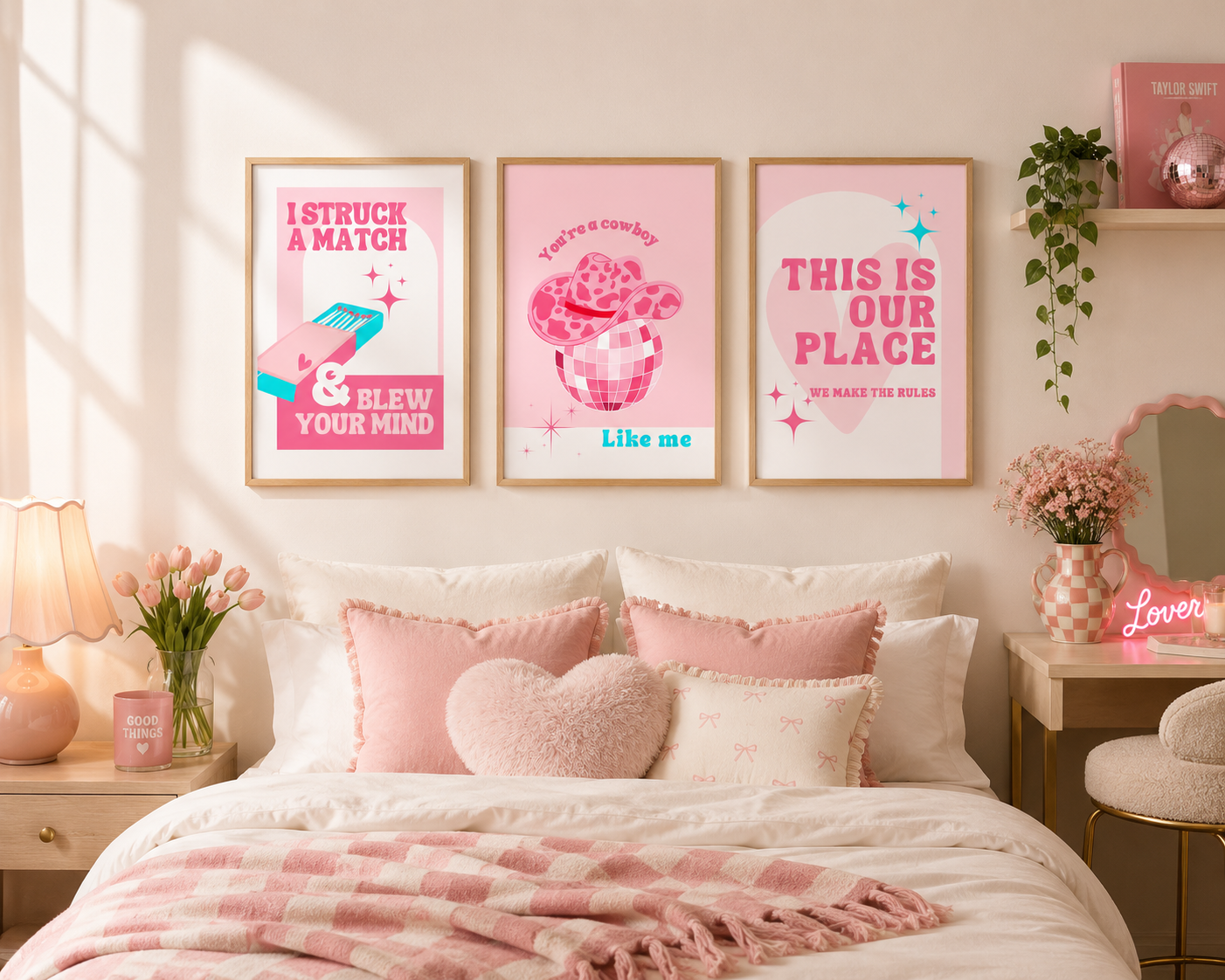 Three framed pink motivational posters hang above a bed in a softly styled bedroom. The posters feature pastel pink graphics and text including 'I STRUCK A MATCH & BLEW YOUR MIND', 'YOU'RE SO COOL LIKE ME', and 'THIS IS OUR PLACE WE MAKE THE RULES'.