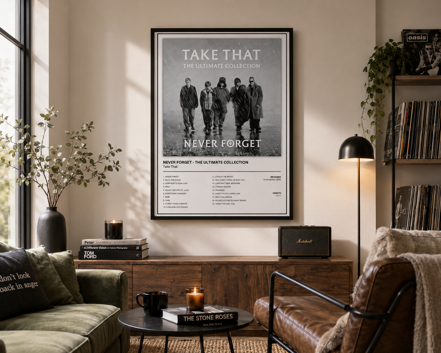 A framed black-and-white music poster  Take That - The Ultimate Collection' hanging on a beige wall in a styled living room with a sofa, chair, table, lamp, and record shelves.
