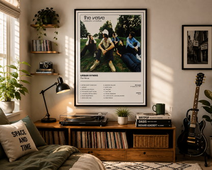 A framed music poster for 'The Velve - Urban Hymns' hangs on a wall in a cozy, sunlit room with a wooden record console, record players, a turntable, books, a guitar, and plants.