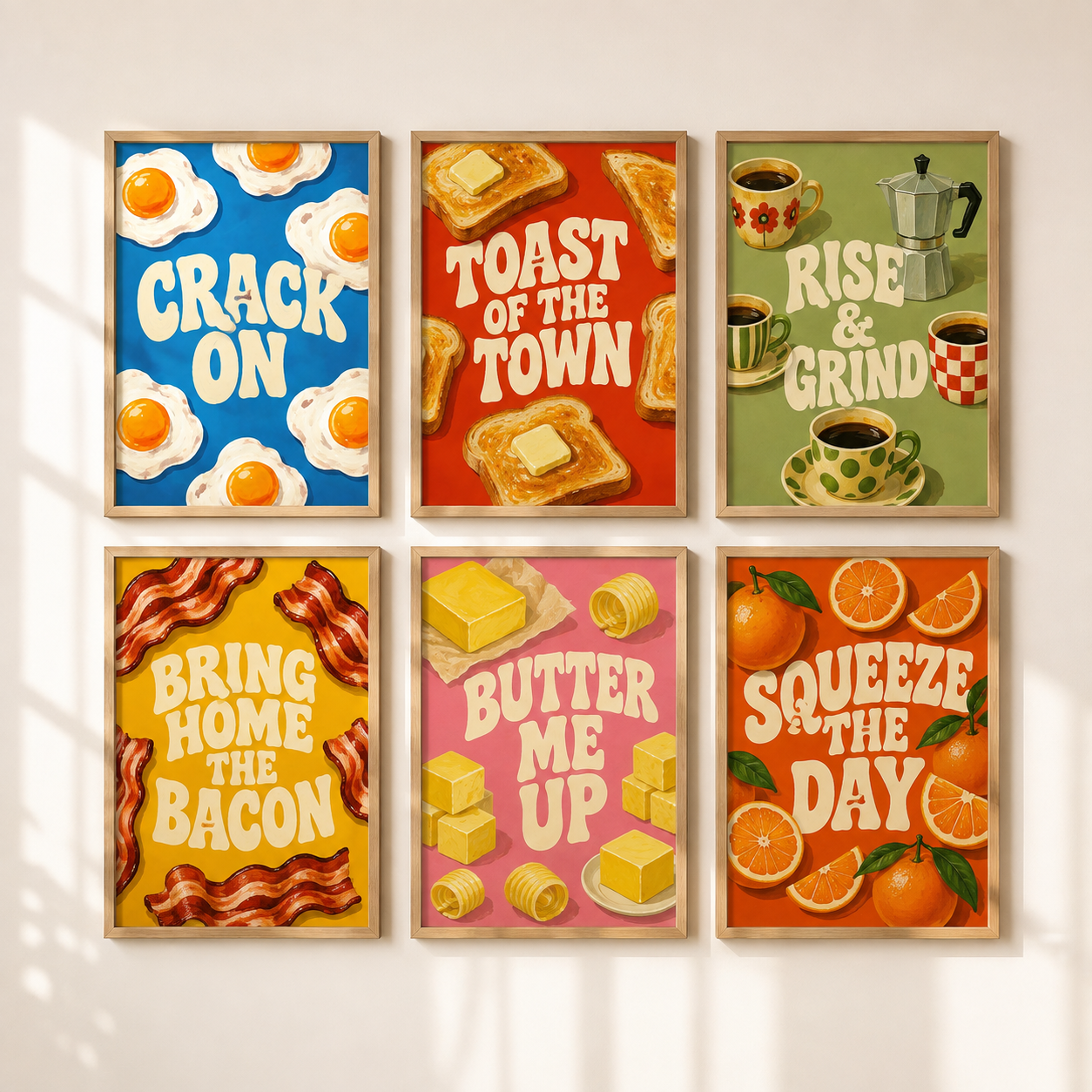Six framed breakfast-themed art prints arranged in a 2x3 grid on a light beige wall with soft window shadows. The prints feature colorful retro designs with text including 'CRACK ON', 'TOAST OF THE TOWN', 'RISE & GRIND', 'BRING HOME THE BACON', 'BUTTER ME UP', and 'SQUEEZE THE DAY', along with illustrations of eggs, toast, coffee cups, bacon, butter, and oranges.