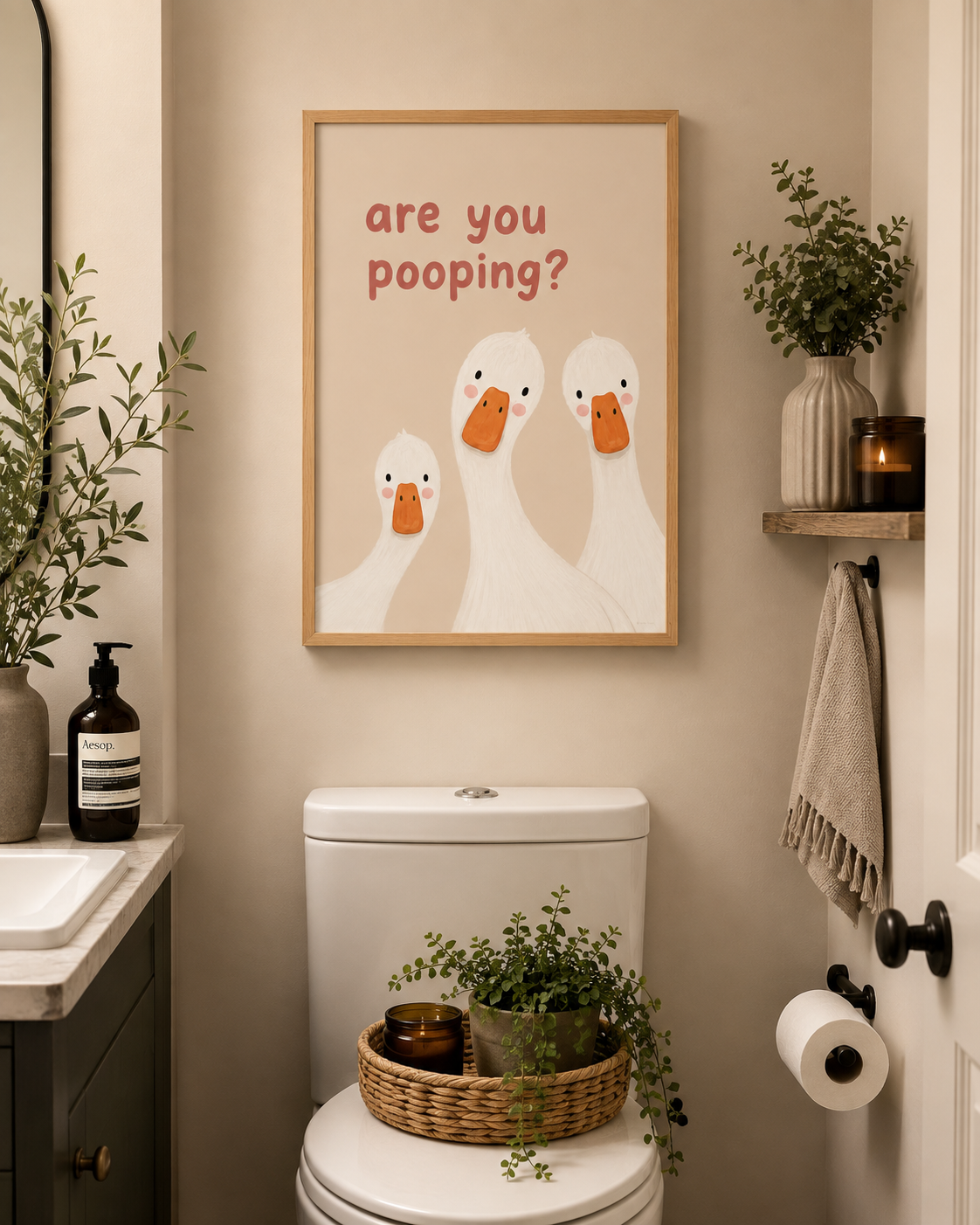 A framed wall art print featuring three cartoon white ducks with orange beaks and the text 'are you pooping?' in red, displayed above a toilet in a styled bathroom setting.