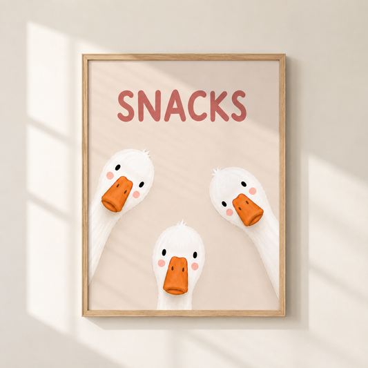 A framed wall art print featuring the word “SNACKS” above three cartoon white ducks with orange beaks, hanging on a light beige wall with soft window-shadow lighting.