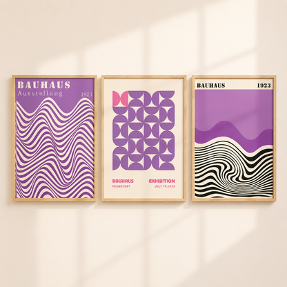 Three framed Bauhaus-style art prints in purple, black, white, and pink, displayed side-by-side on a warm beige wall with soft window shadows.