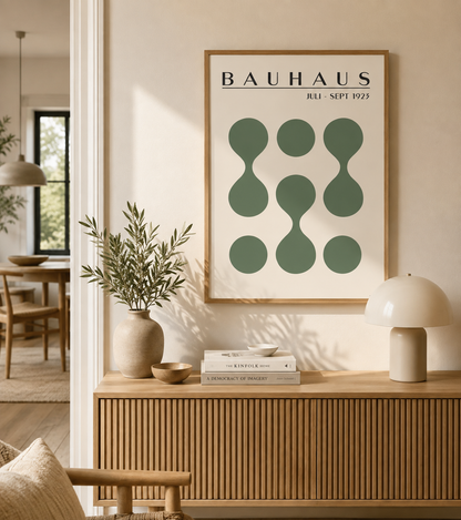 A framed Bauhaus wall art print hangs on a beige wall above a wooden console table in a styled interior. The poster features dark green abstract geometric shapes on a white background with the text 'BAUHAUS 1911 - 1925' at the top.