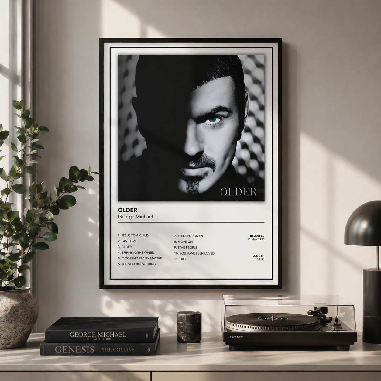 A framed black-and-white music poster of George Michael titled 'OLDER' hangs on a light beige wall above a console table with books, a turntable, and a lamp in a styled interior setting.