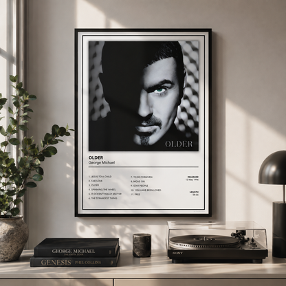 A framed black-and-white music poster of George Michael titled 'OLDER' hangs on a light beige wall above a console table with books, a turntable, and a lamp in a styled interior setting.