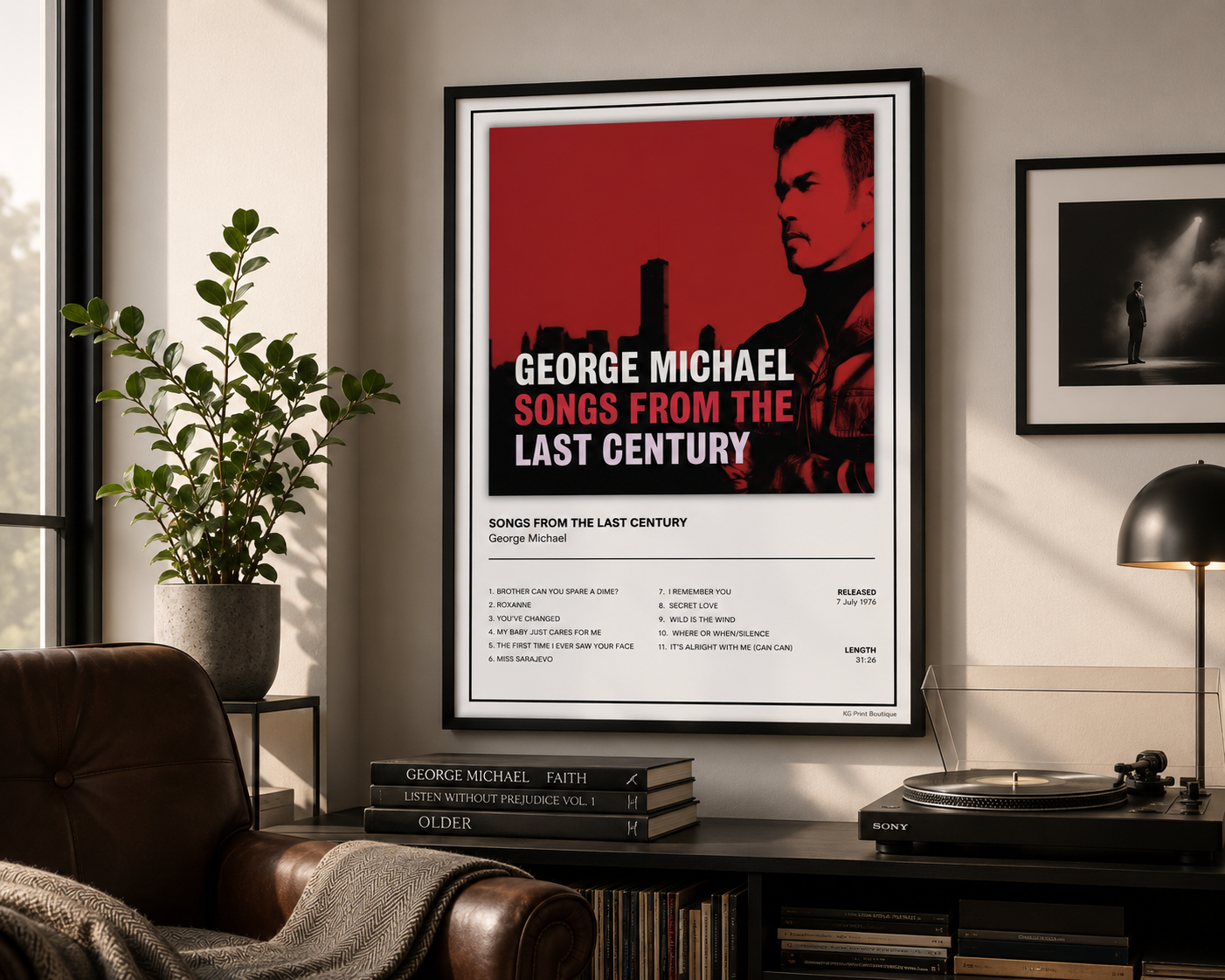 A framed music poster for George Michael's 'Songs from the Last Century' hanging on a wall in a modern living room setting with a leather armchair, plant, and turntable visible.