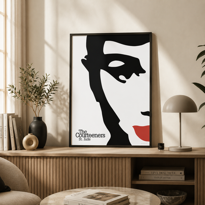 A framed art print featuring a stylized black and white portrait of a woman with red lips and the text 'The Courteeners St. Jude' is displayed on a wooden console table in a modern, sunlit living room.