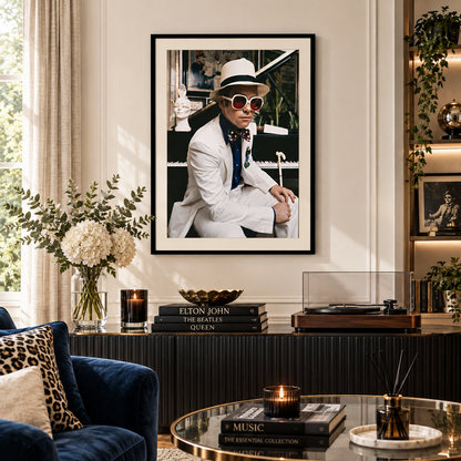 A large framed black-and-white art print of Elton John in a white suit and hat hangs on a cream wall above a console table in a modern, elegantly decorated living room.