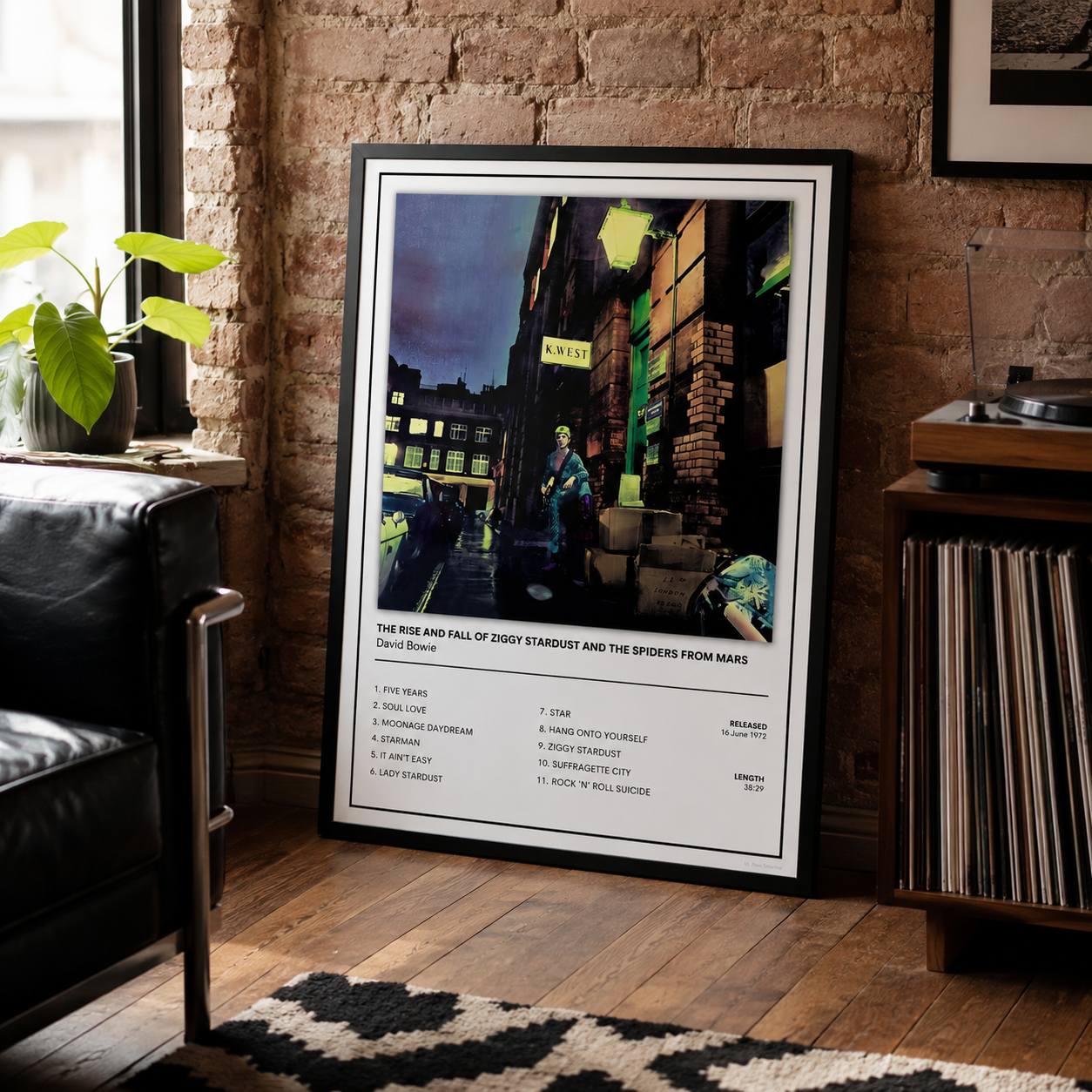 A framed music poster for David Bowie's 'The Road and Fall of Ziggy Stardust and the Spiders from Mars' is displayed leaning against a rustic brick wall in a cozy room setting with a leather chair, plant, and record player.