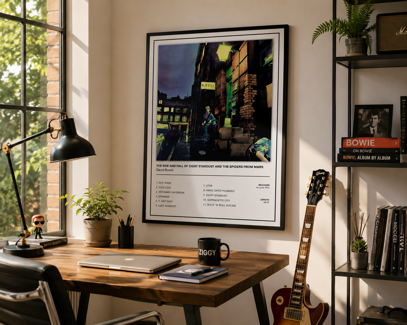 A framed music poster of David Bowie's 'The Rise and Fall of Ziggy Stardust and the Spiders from Mars' displayed on a wall in a styled home office setting with a desk, lamp, and guitar.