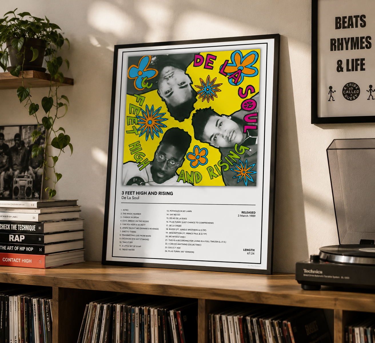 A framed music poster for De La Soul's '3 Feet High and Rising' displayed on a wooden shelf in a styled room setting with a record player, vinyl records, and another framed print.
