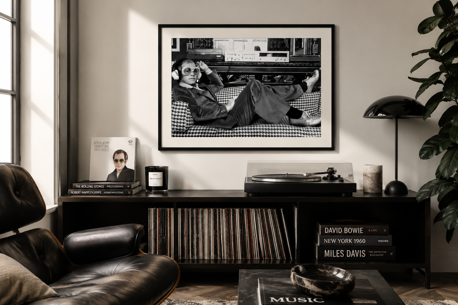 A framed black-and-white art print of Elton John lounging on a couch, displayed on a wall above a dark media console in a modern living room setting.