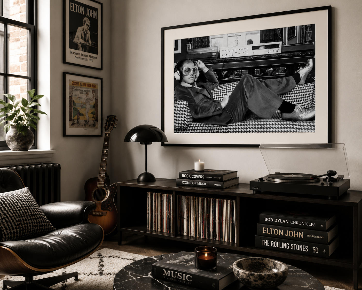 A large black and white framed art print of Elton John lounging on a couch hangs on a wall in a styled living room. The room features a black leather armchair, a wooden console table with a turntable and records, a guitar leaning against the wall, and other framed music posters.