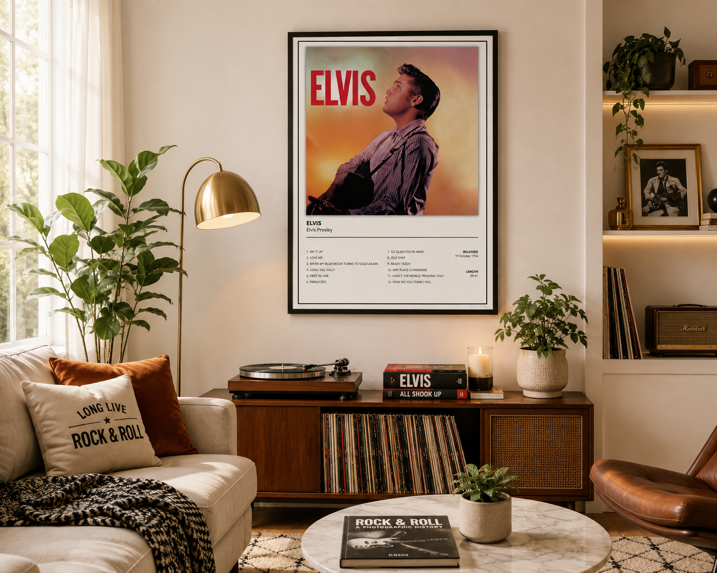A framed Elvis Presley poster hangs on a beige wall in a styled living room with a sofa, lamp, plants, records, and shelving.