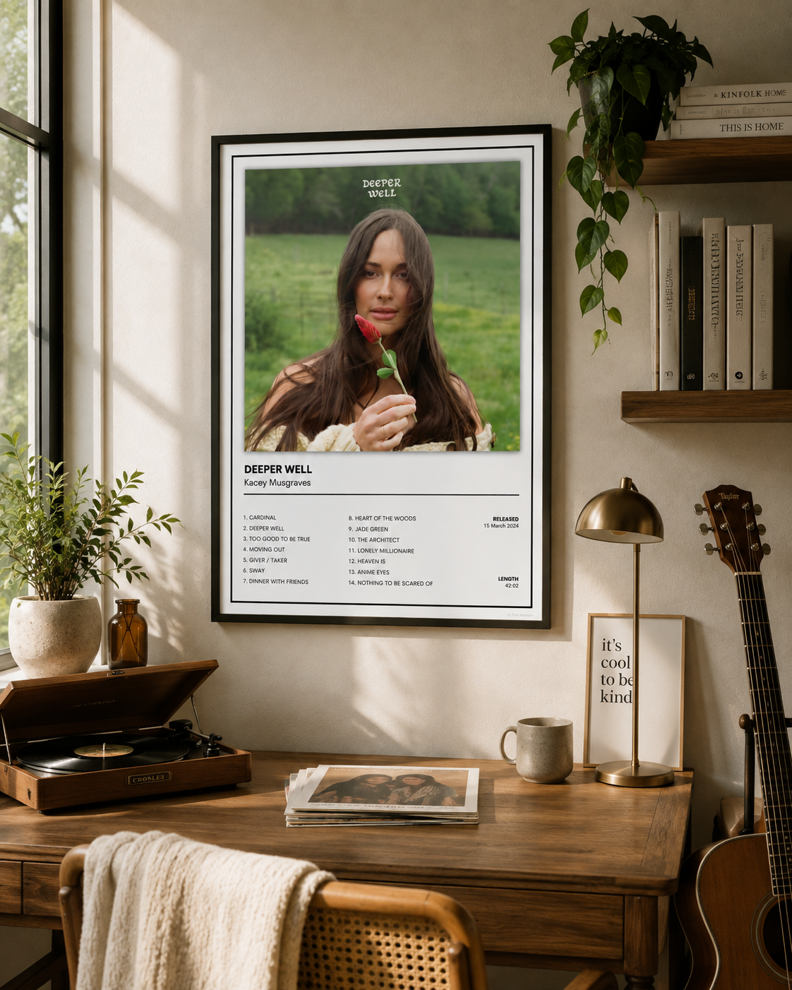 A framed music poster for Kacey Musgraves – Deeper Well hangs on a wall in a styled home office setting with a desk, plants, and a guitar.