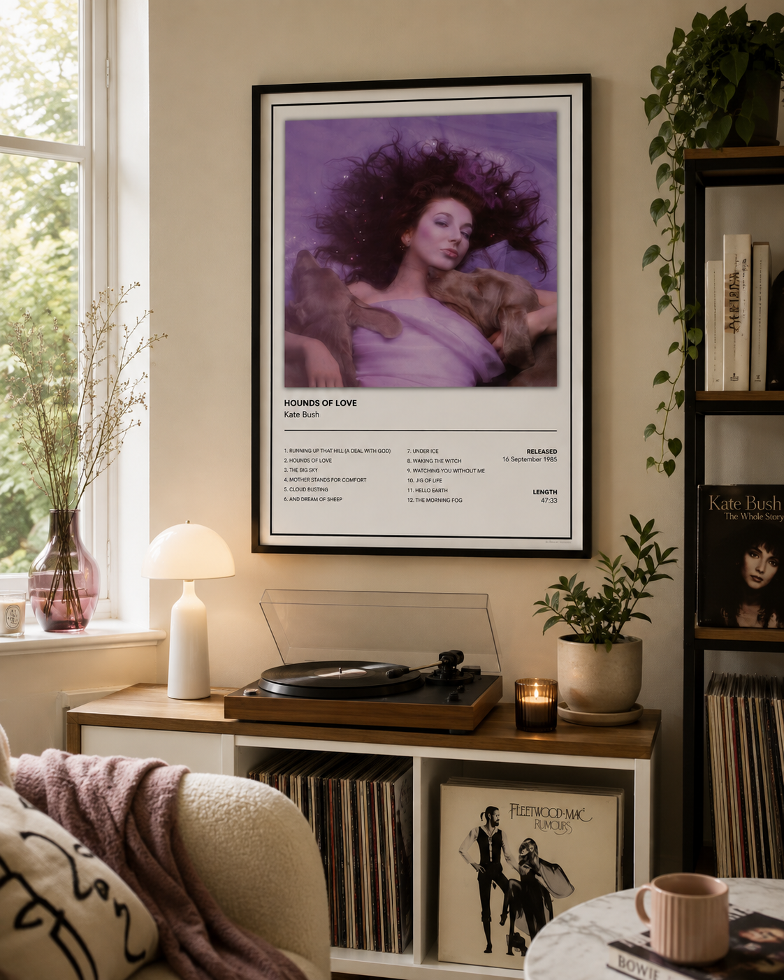 A framed Kate Bush – 'Hounds of Love' music poster hangs on a beige wall in a cozy, sunlit living room above a wooden console table with a turntable, plants, and vinyl records.