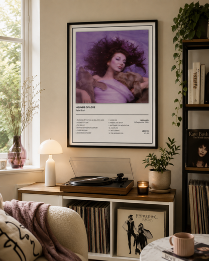 A framed Kate Bush – 'Hounds of Love' music poster hangs on a beige wall in a cozy, sunlit living room above a wooden console table with a turntable, plants, and vinyl records.