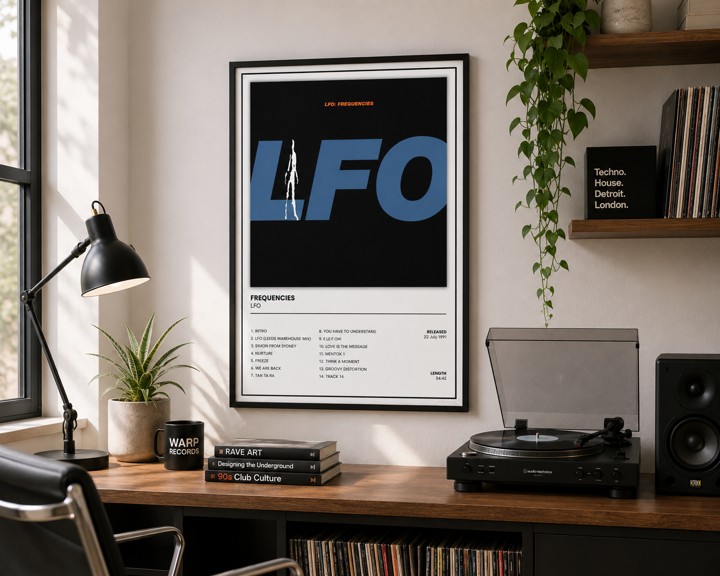 A framed LFO music poster hangs on a wall above a wooden desk in a styled home office setting. The desk includes a black desk lamp, a potted plant, a turntable, a speaker, and vinyl records.