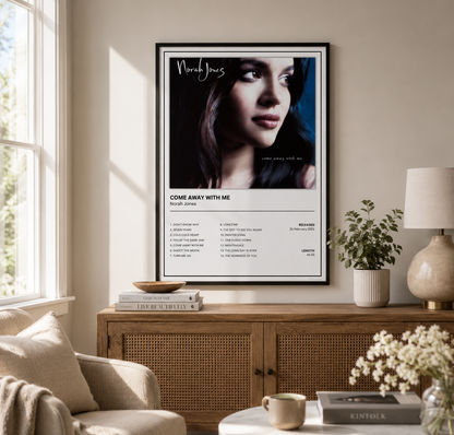 A framed music poster of North Jones featuring the song 'Come Away With Me' is displayed on a beige wall in a styled living room setting above a wooden cabinet.