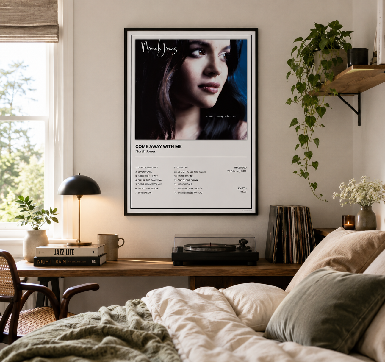 A framed music poster for Norah Jones's song 'Come Away With Me' displayed on a bedroom wall above a wooden desk with a lamp, records, and a bed with cream bedding.