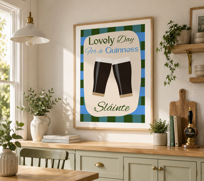 A framed wall art print hangs above a kitchen counter. The print features a blue and green plaid background with the text 'Lovely Day for a Guinness' and 'Sláinte' in stylized lettering, plus an illustration of two pint glasses.