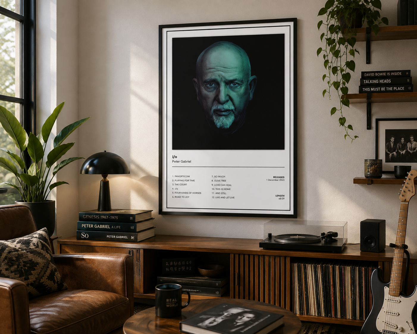 A framed black-and-white poster of Peter Gabriel i/o hanging on a wall in a styled living room with a leather chair, record player, plants, and shelves.