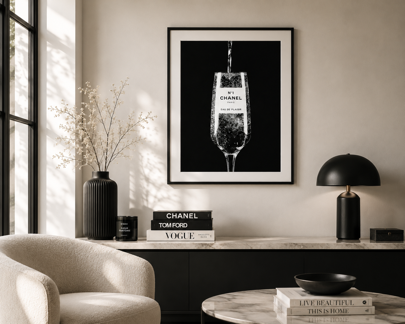 A framed black and white art print of a Chanel champagne flute hanging on a beige wall in a modern, sunlit living room setting.