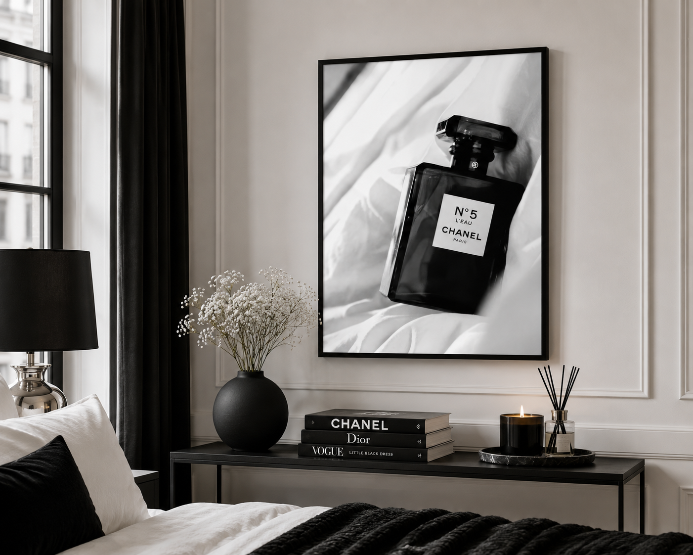 A framed black and white art print of a Chanel No. 5 perfume bottle hanging on a light gray wall above a bed in a modern bedroom setting.