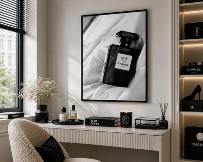 A framed black and white art print of a Chanel No. 5 perfume bottle hanging on a wall above a console table in a modern, stylishly decorated room.