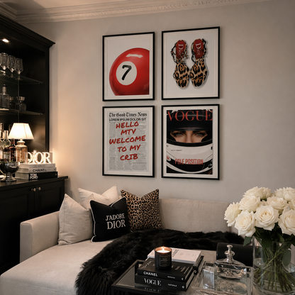 A styled interior scene showing four framed wall art prints above a sofa. The prints feature a red billiard ball with the number 7, leopard-print shoes, a fashion quote poster, and a Vogue magazine cover with a racing helmet.