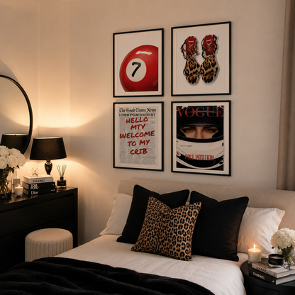 A styled bedroom interior showing a bed with black and leopard-print pillows, framed wall art above the headboard, a bedside table with lamps and books, and a mirror on the left.
