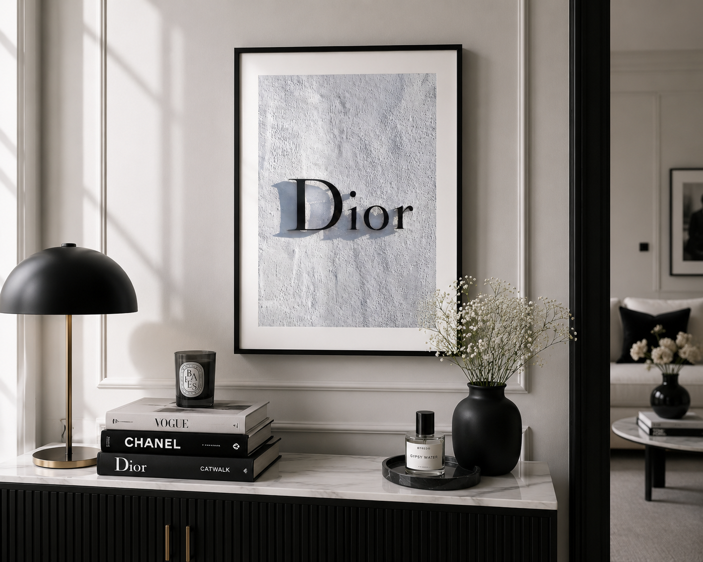 A framed art print featuring the Dior logo on a textured light gray background, displayed on a white wall above a console table in a modern, stylishly decorated room.