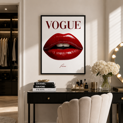 A framed Vogue poster featuring a close-up of glossy red lips hangs on a beige wall above a black vanity table with perfume bottles, a vase of white flowers, and a cream shell chair. A closet is visible on the left.