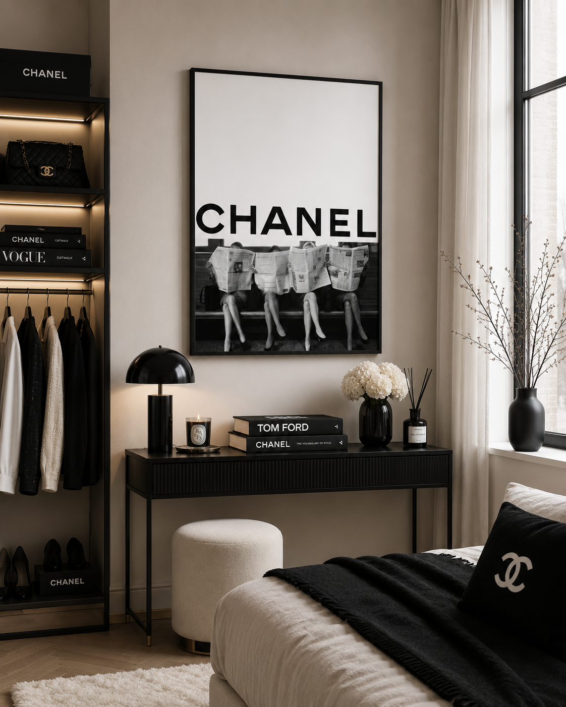 A black and white framed poster with the word CHANEL hangs on a beige wall above a dark console table in a styled bedroom. The room includes a bed with a black throw blanket, a white pouf, shelving with fashion items, and a window with sheer curtains.