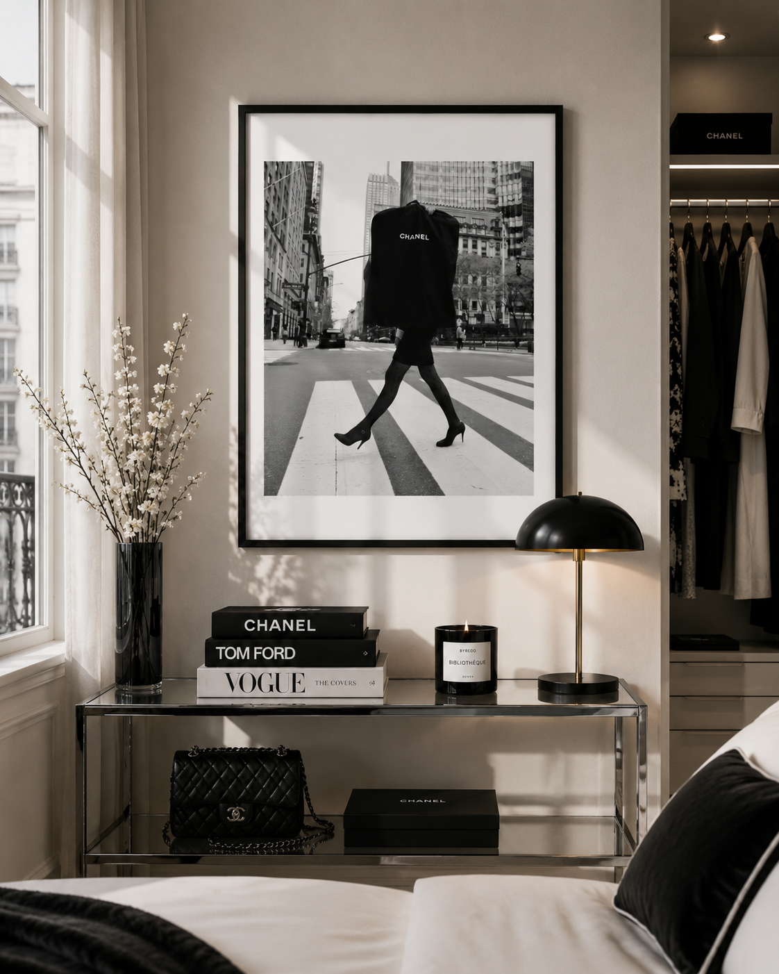 A framed black and white fashion art print of a model walking on a city crosswalk, displayed on a beige wall above a glass console table in a styled bedroom setting.